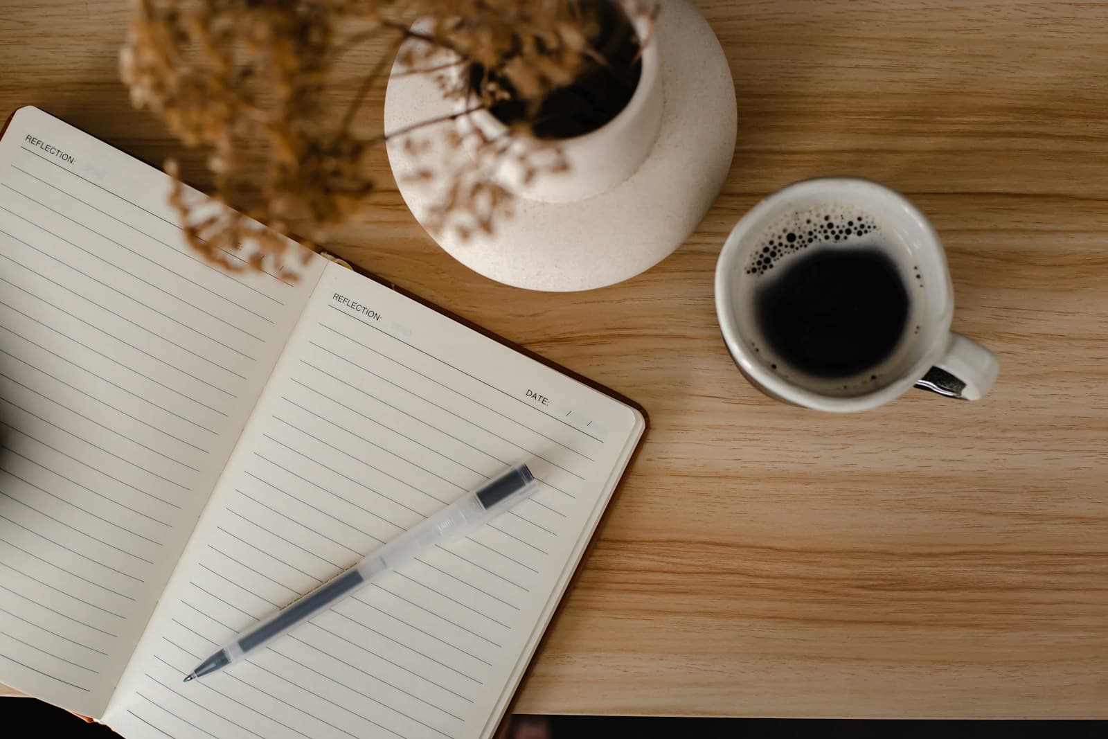 A flat-lay overhead shot of an open notebook with a pen and a cup of coffee
