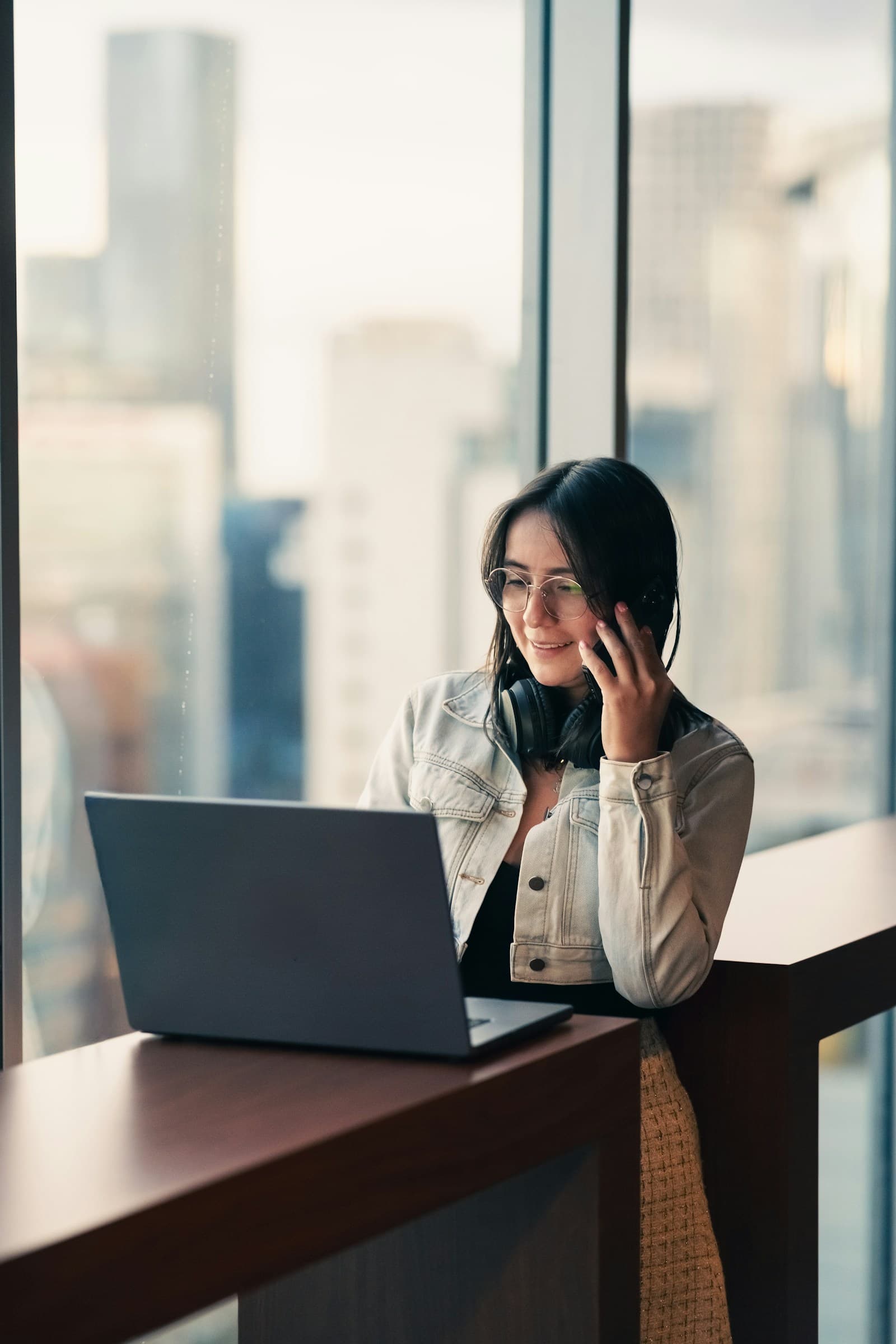A person on a phone call with a laptop open, with city skyline in the window behind