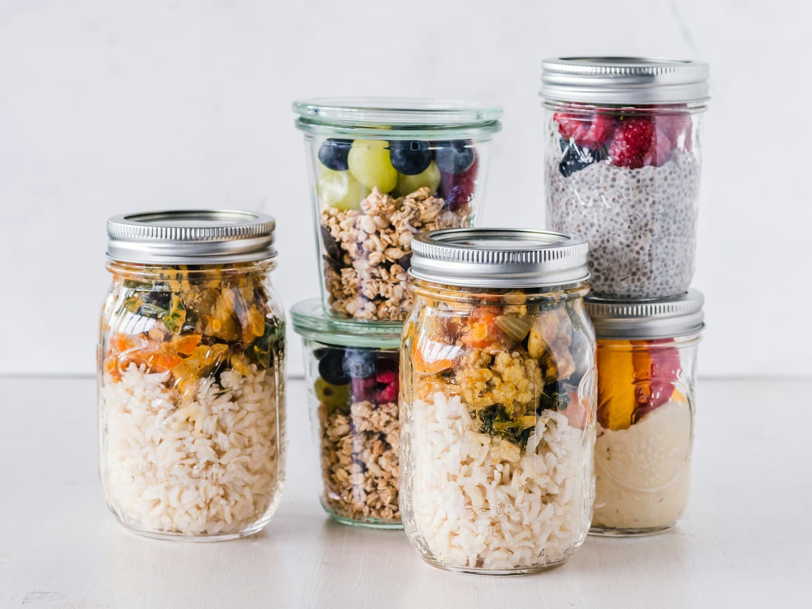 A grouping of glass mason jars filled with prepped grains, fruit, and chia pudding