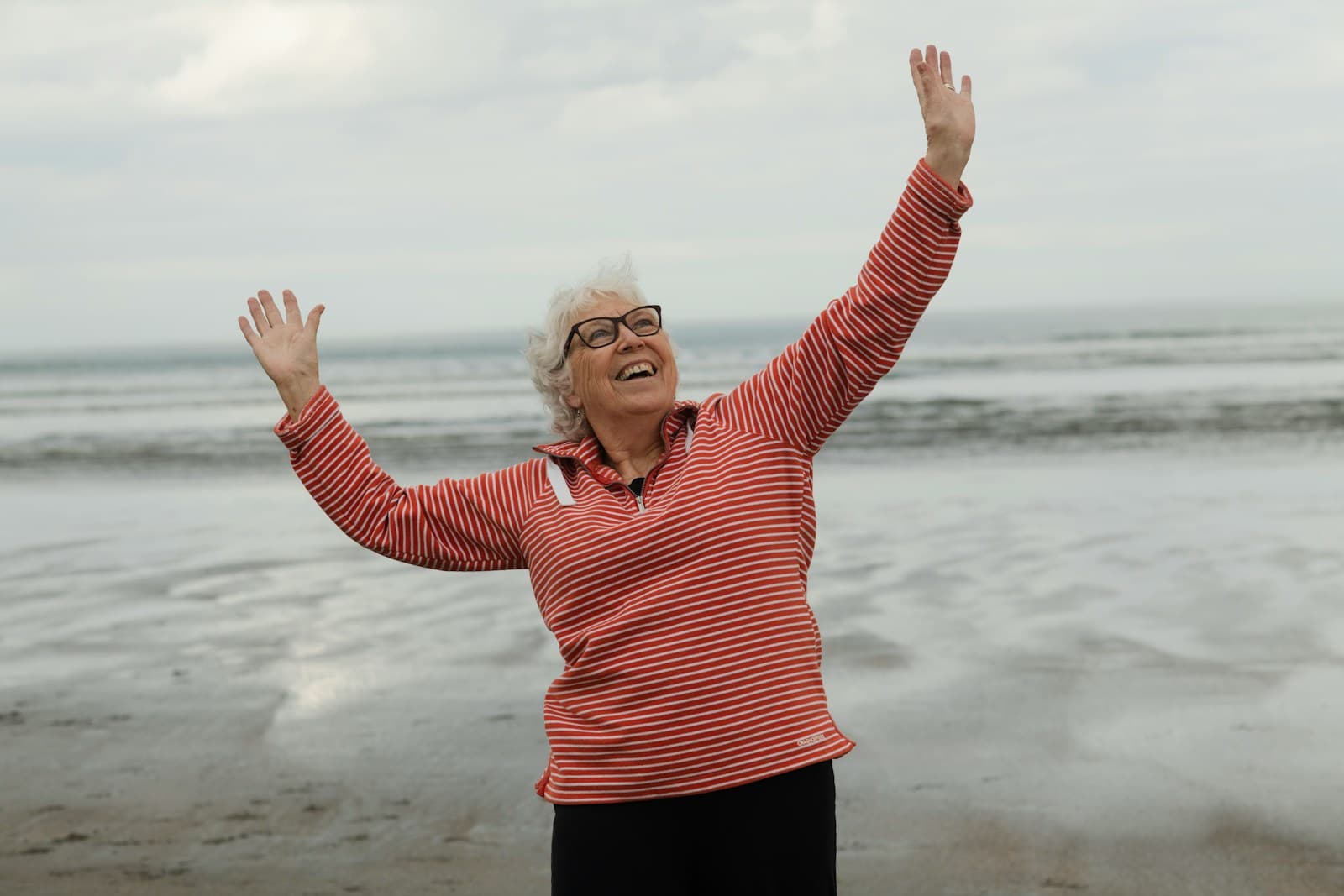 An older woman raising her arms with joy at the beach