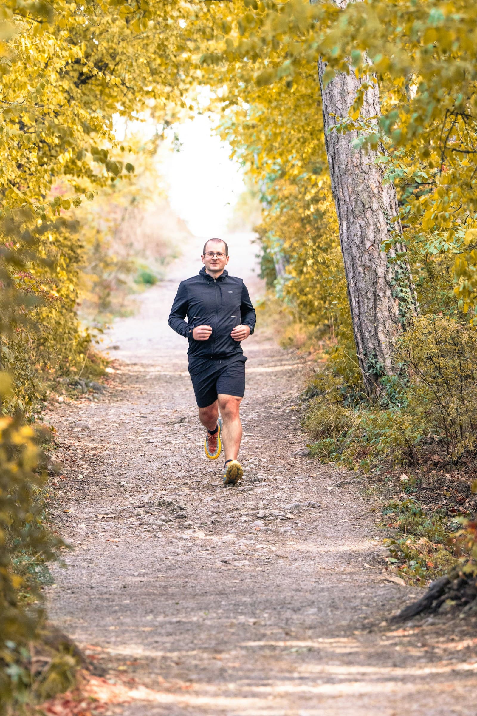 An older man jogging on a tree-lined trail in autumn light
