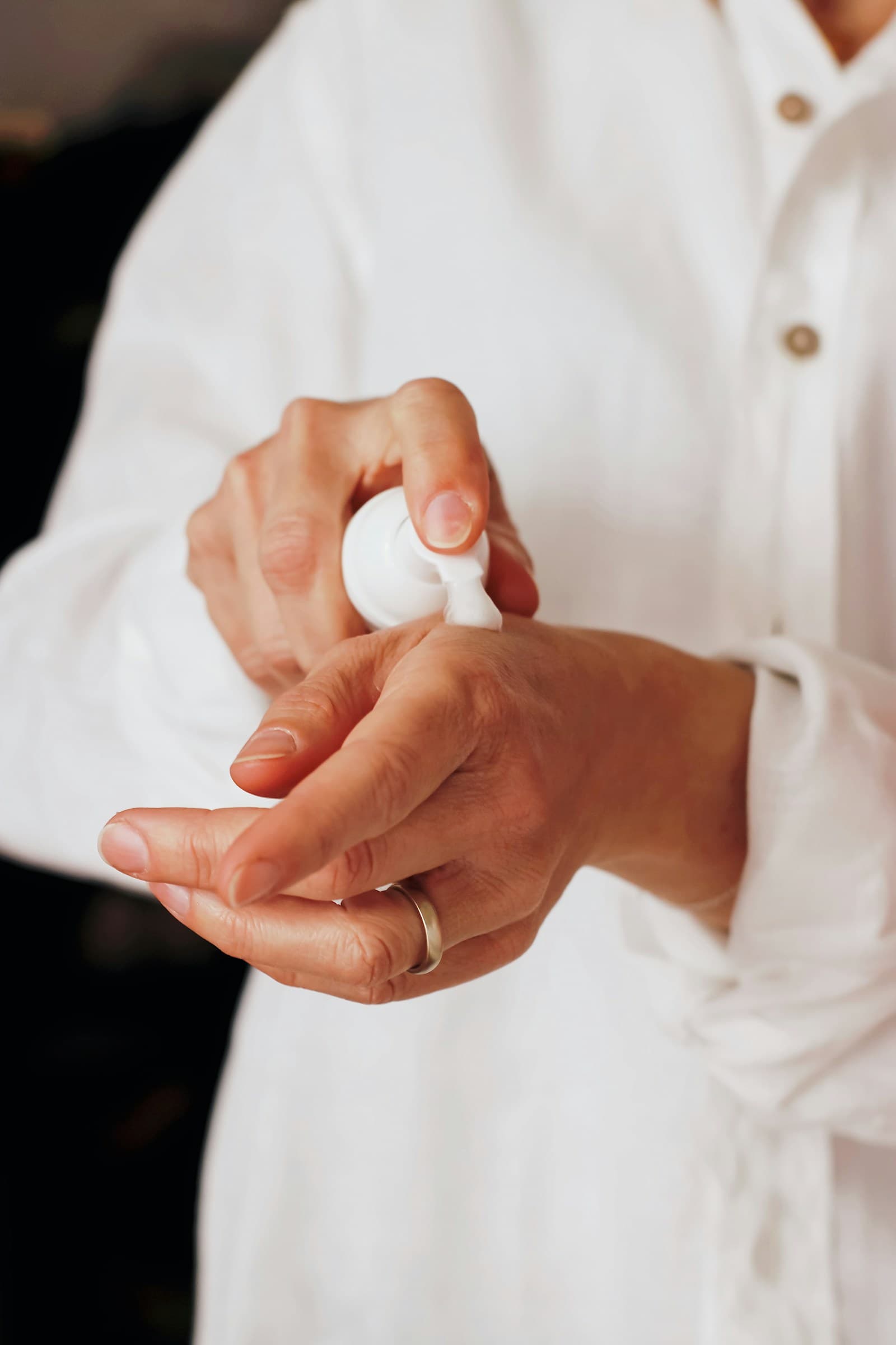 Hands applying skincare from a small white pump bottle