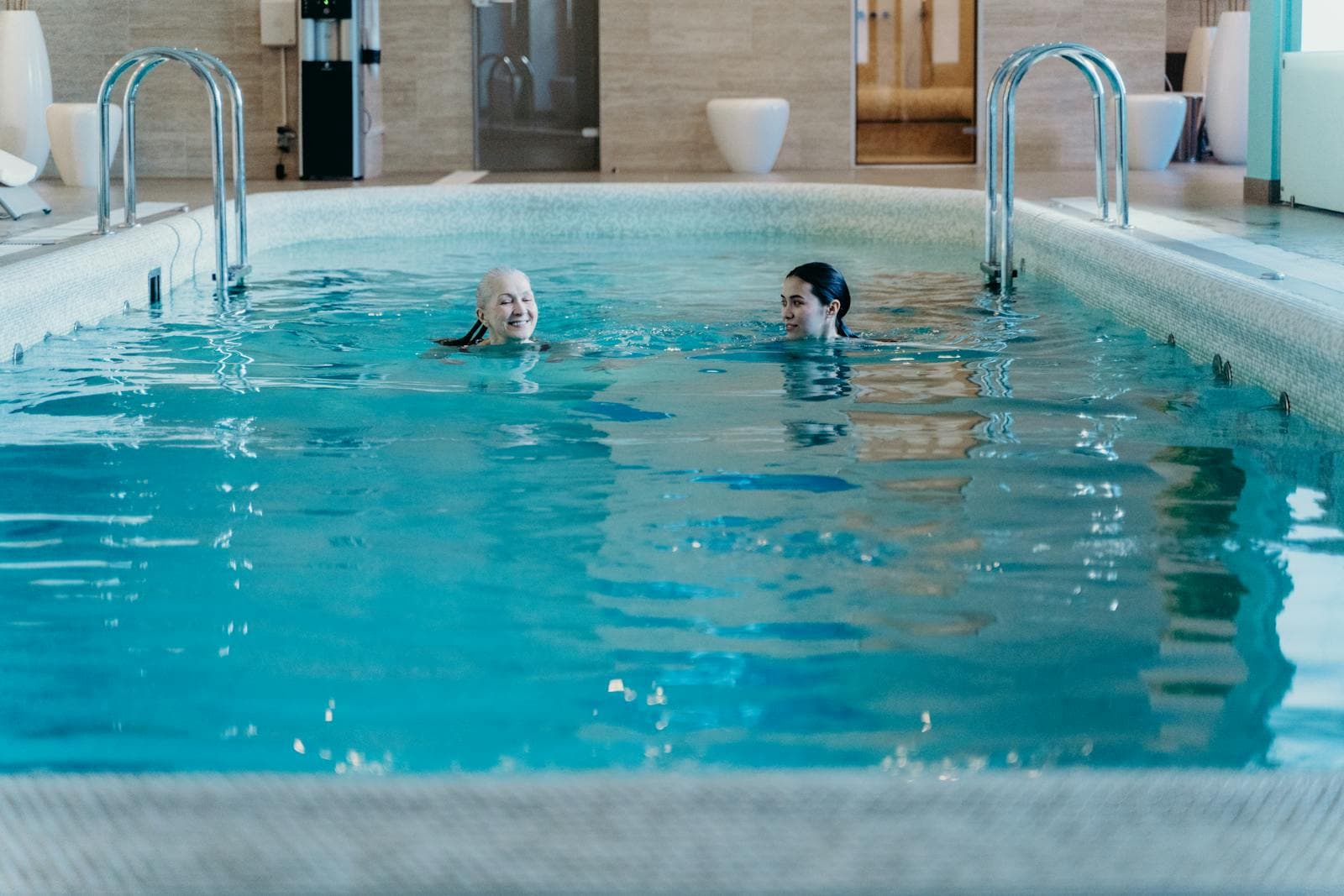 A senior and an adult woman enjoying a swim together at an indoor pool
