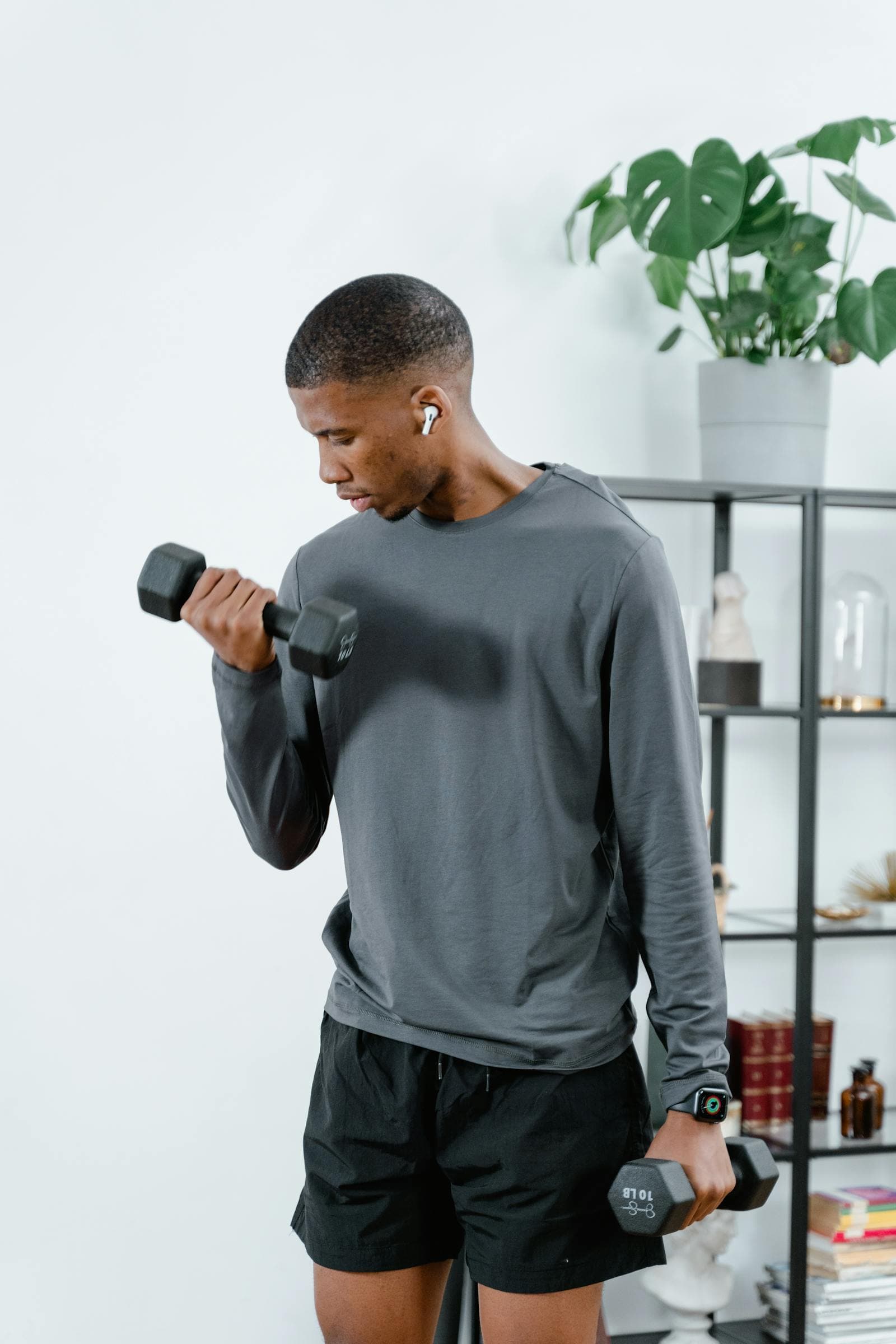 A man lifting a dumbbell at home near a bookshelf and houseplant