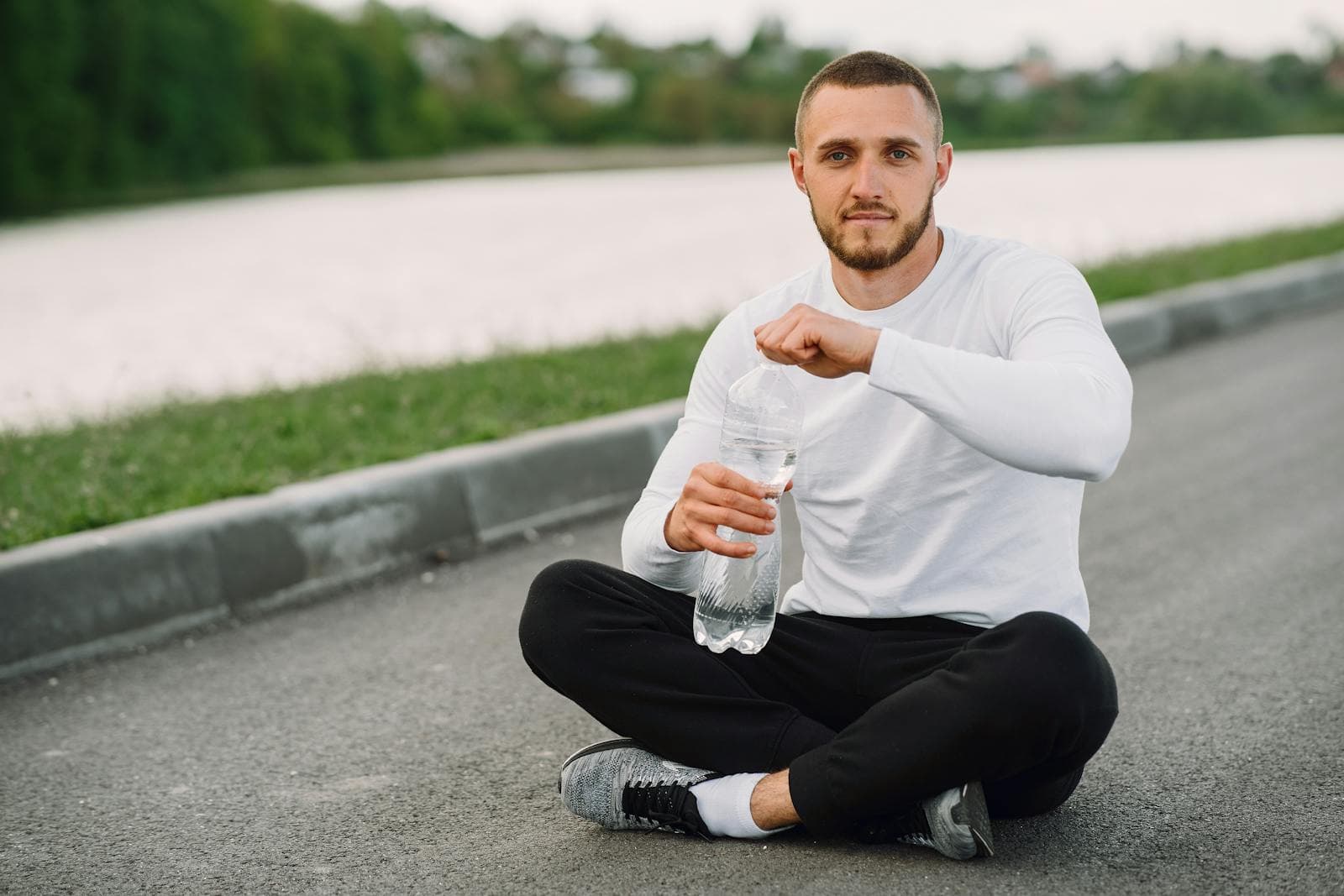 A man sitting outdoors taking a hydration break with a water bottle