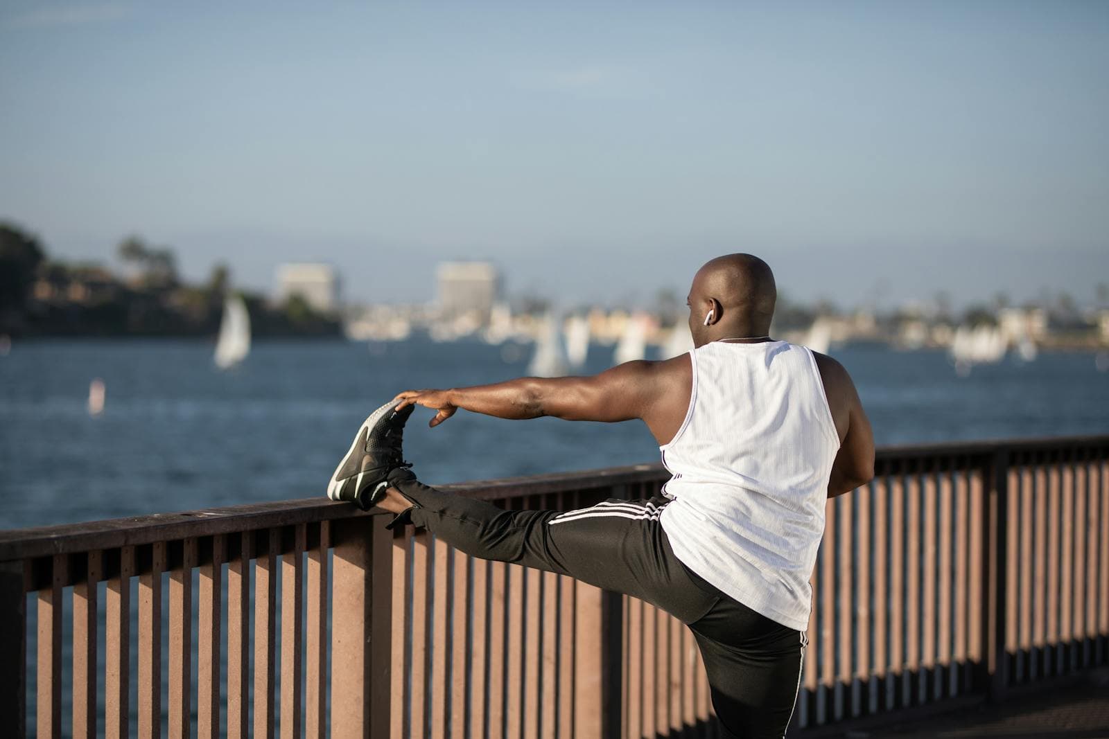 A man stretching his leg on a waterfront railing, city skyline behind him