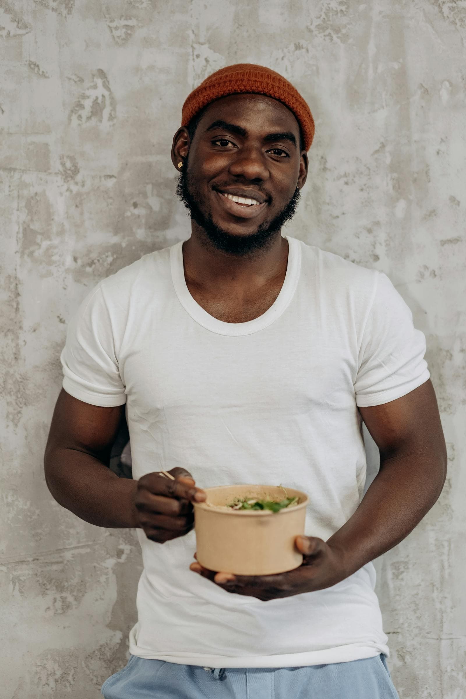 A smiling man holding a bowl of fresh salad greens