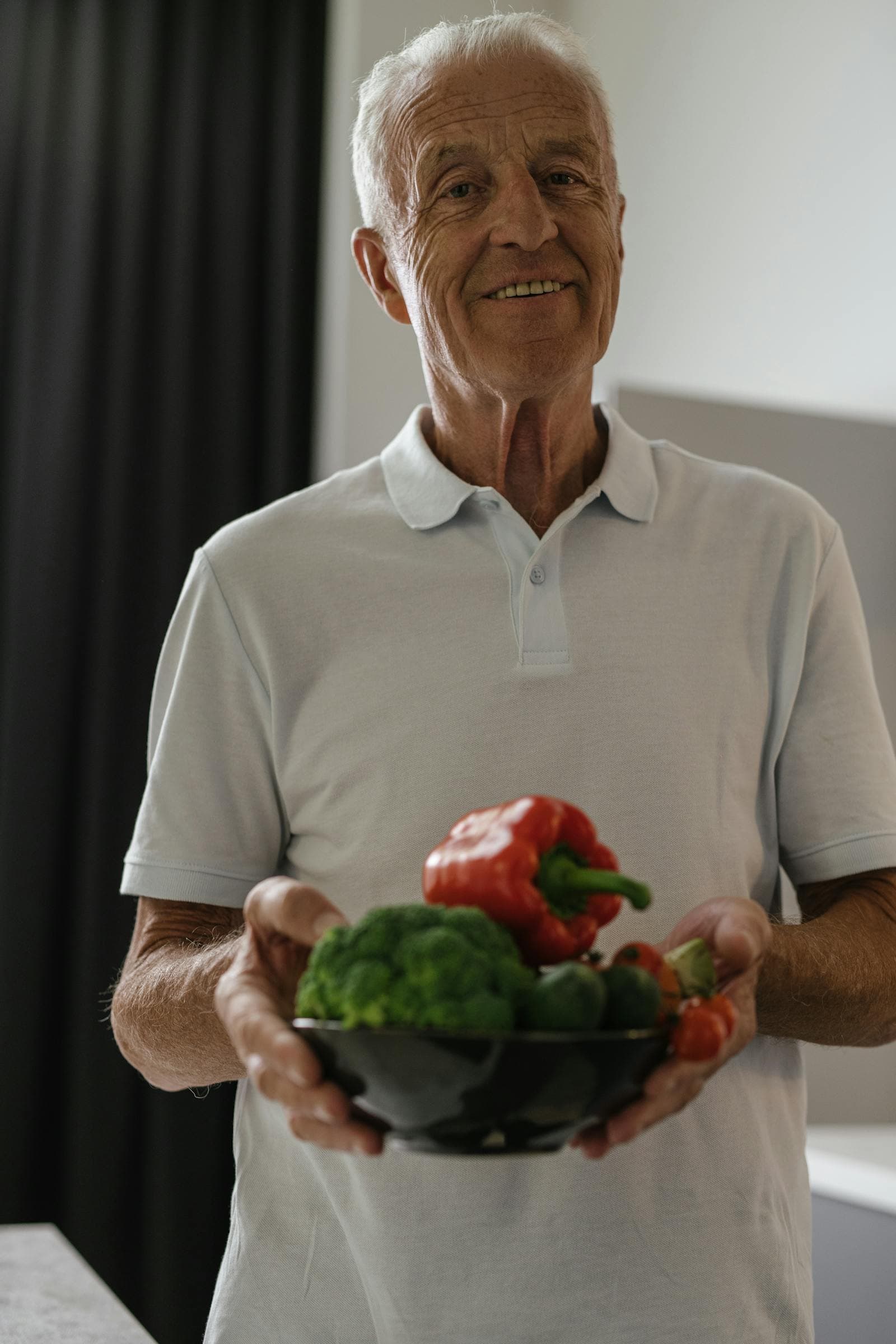 An older man smiling while holding a bowl of fresh vegetables