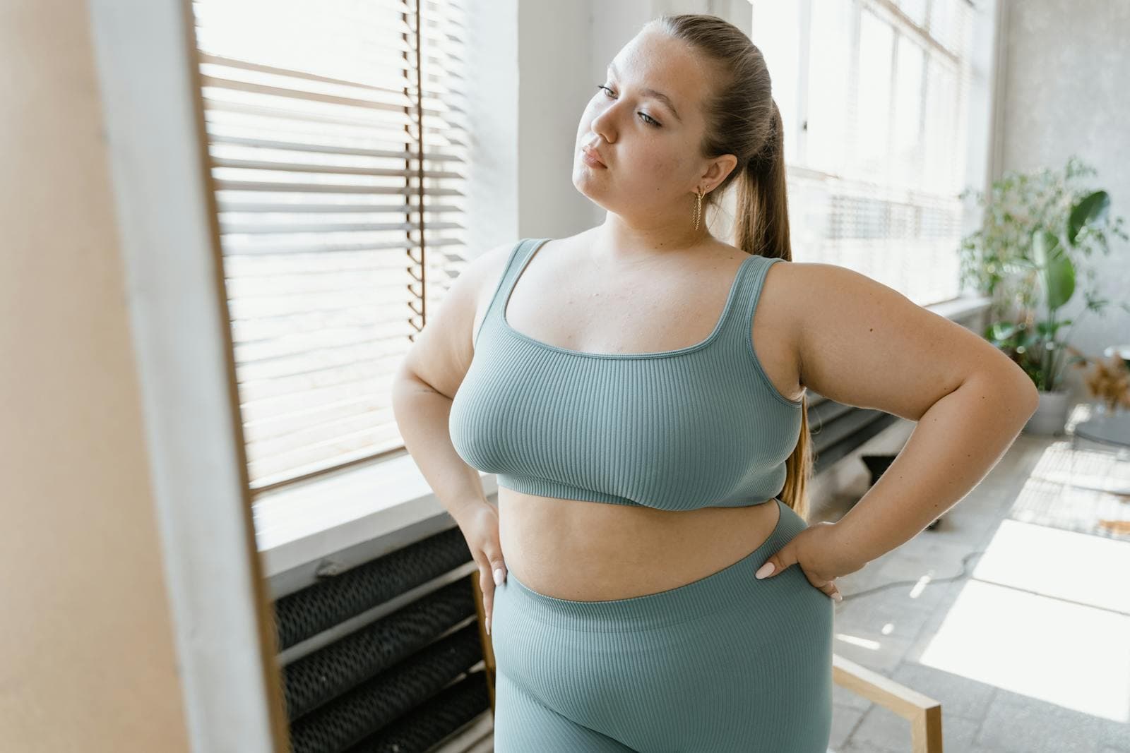 A woman in activewear posing confidently by a sunlit window