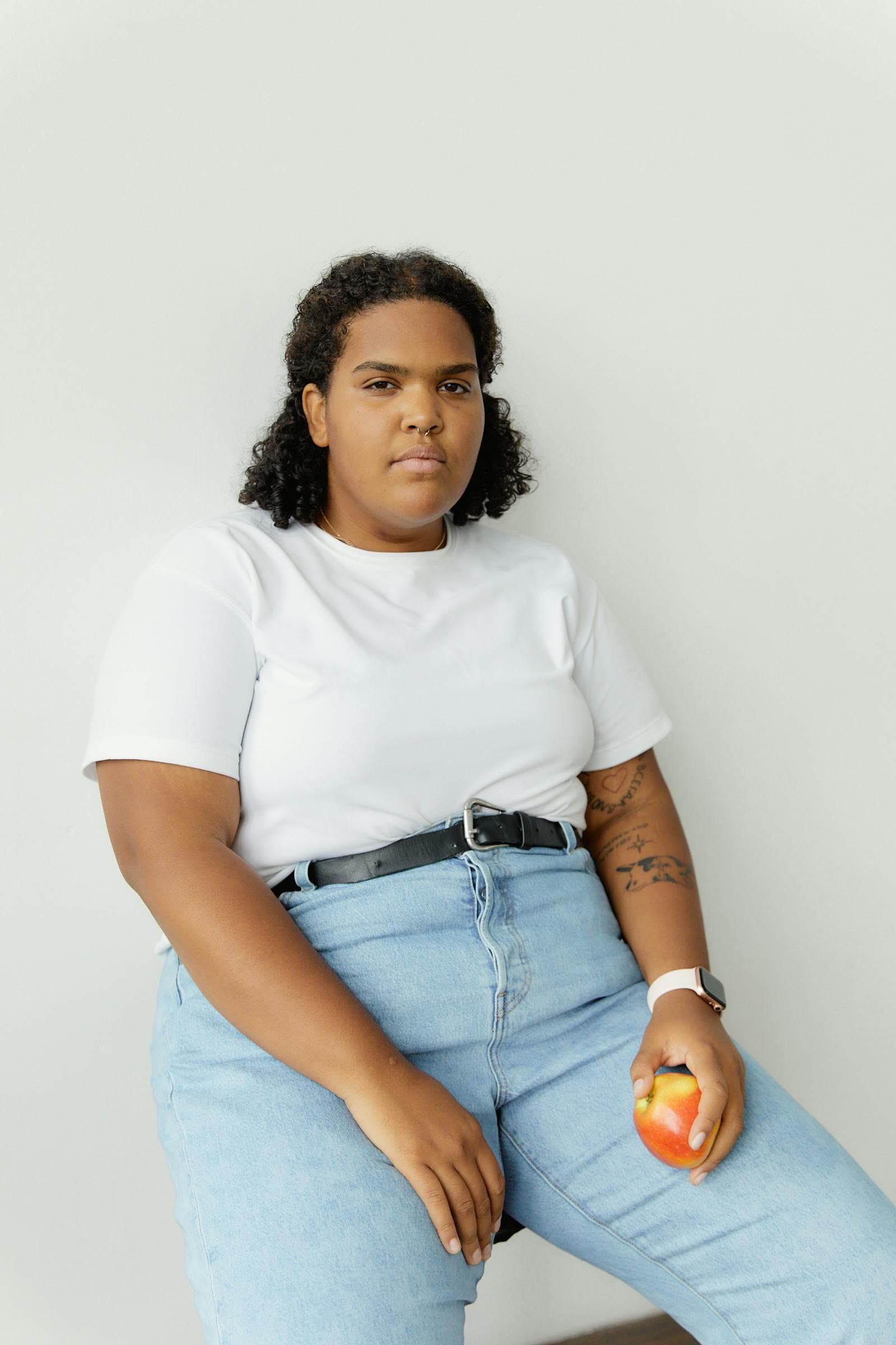 A woman in casual wear holding an apple, seated portrait