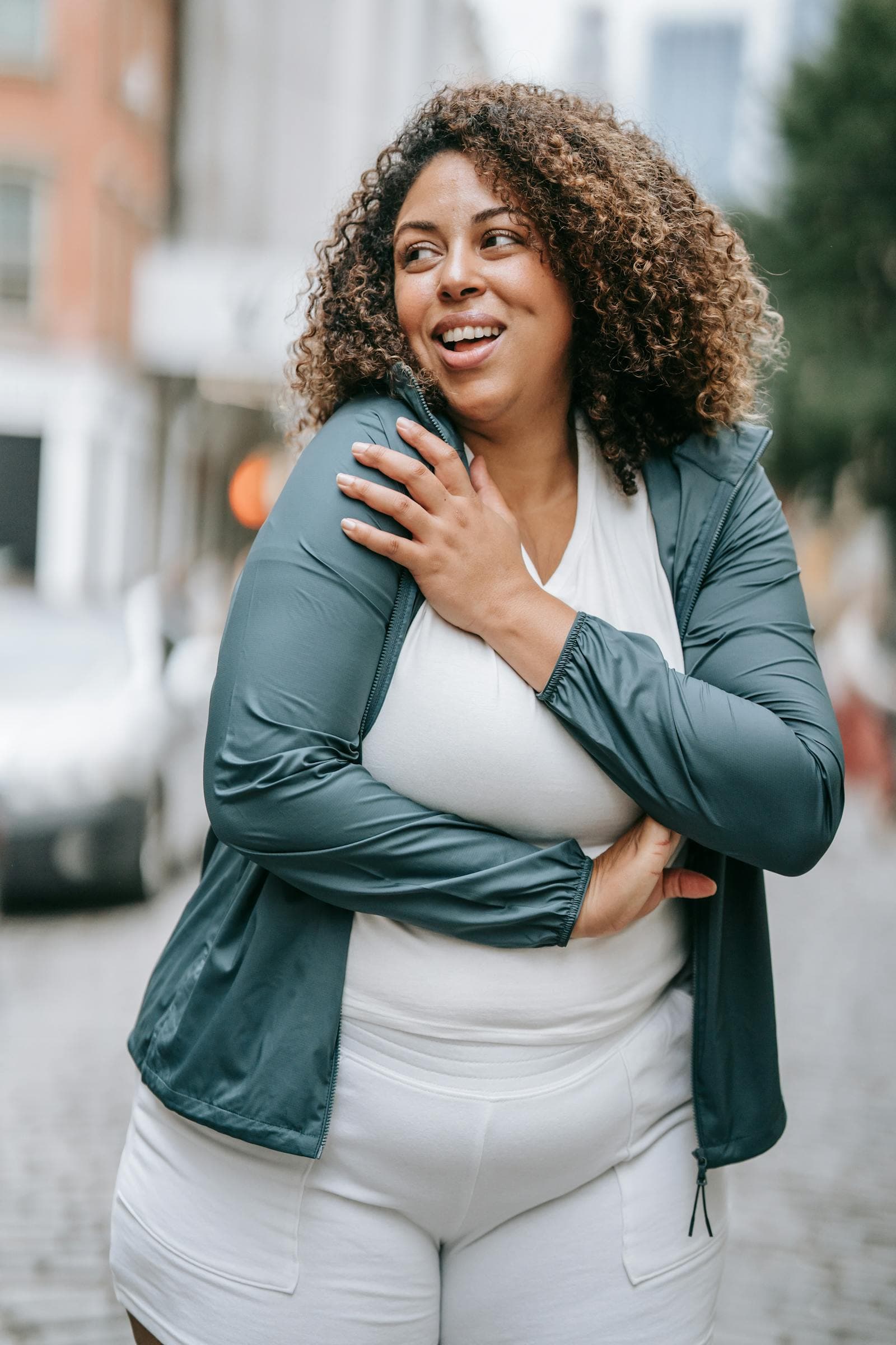 A woman laughing on a city street, hand on her shoulder