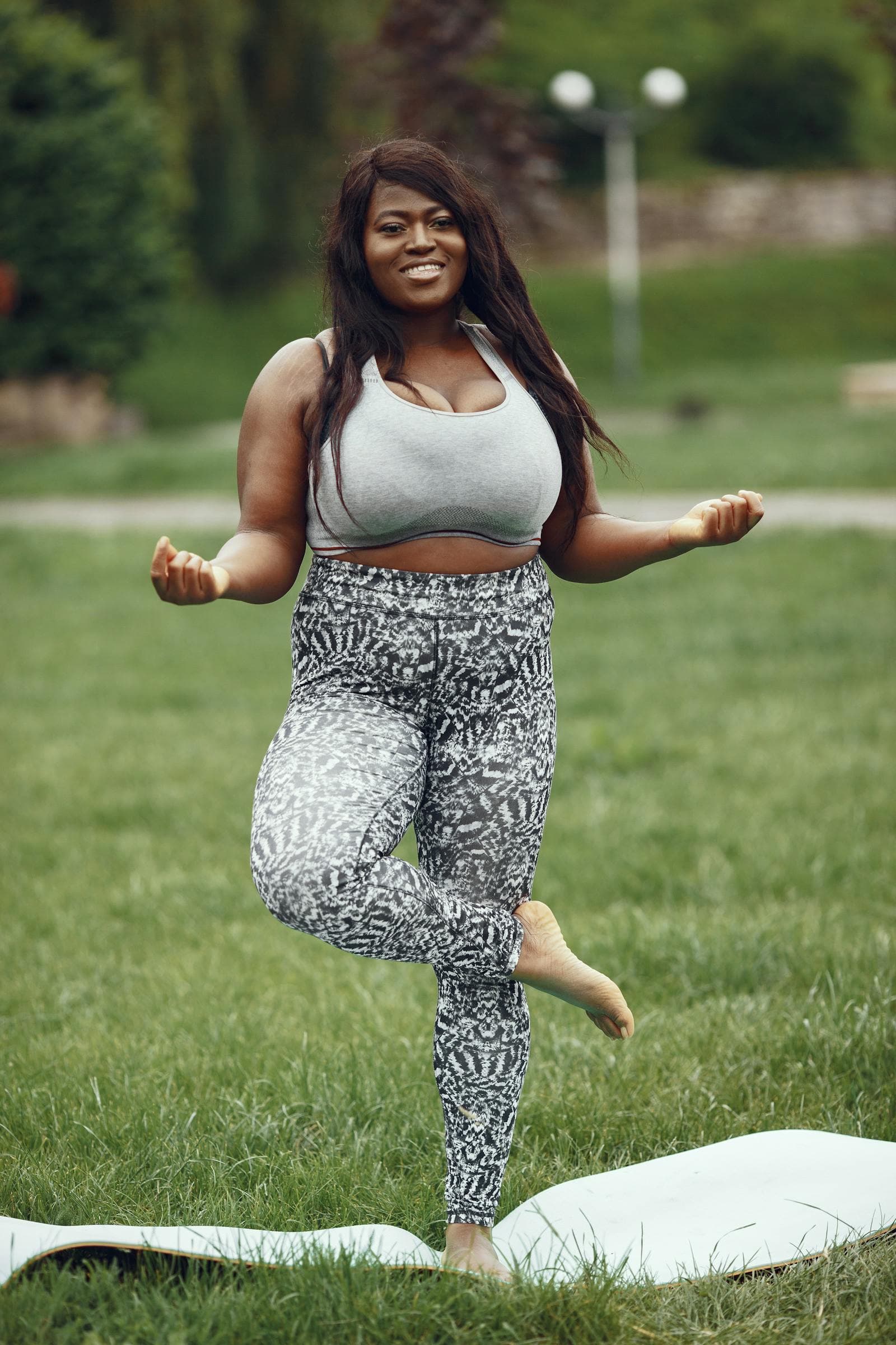 A woman balancing in a yoga tree pose on a grassy field