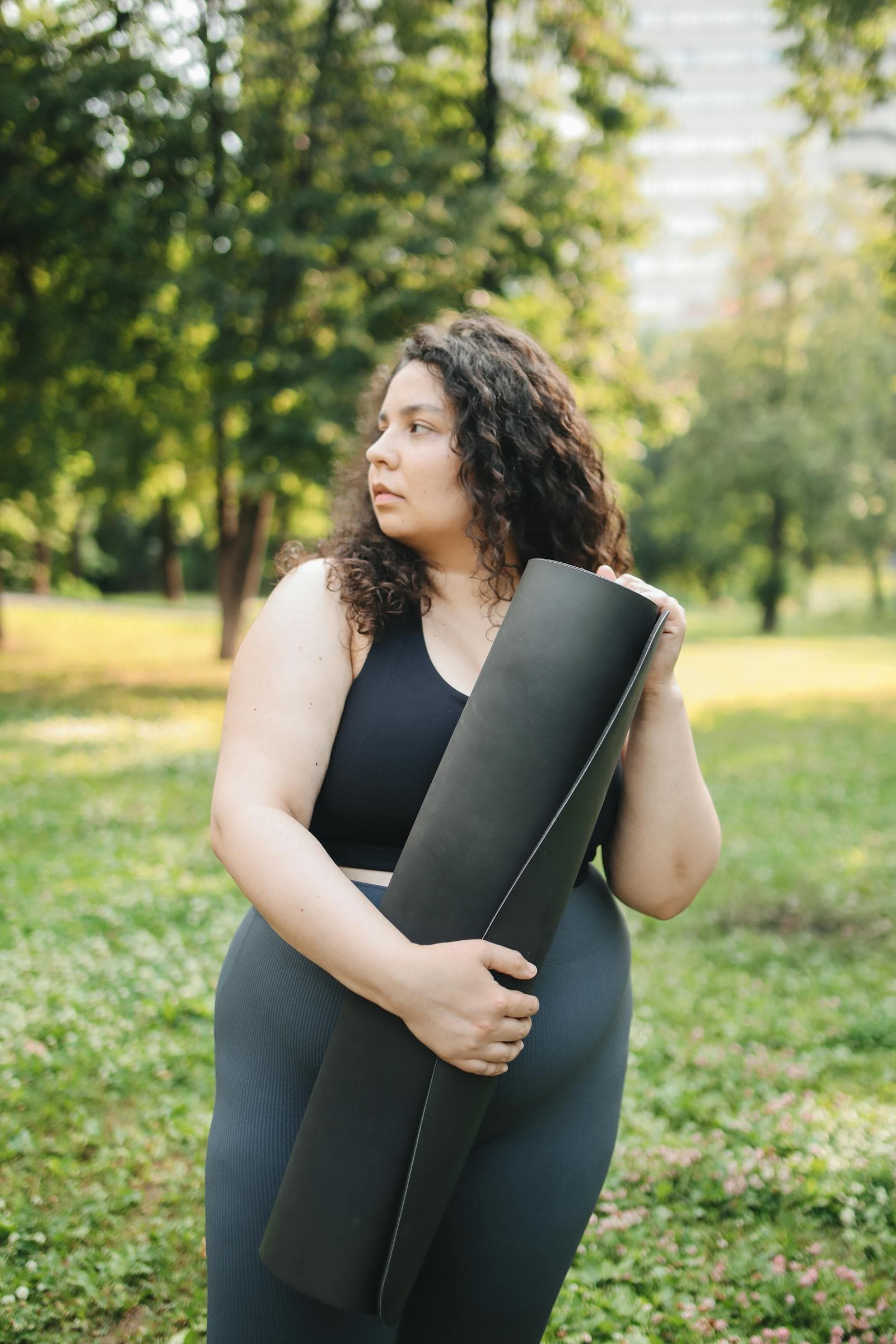 A woman holding a rolled yoga mat in a city park